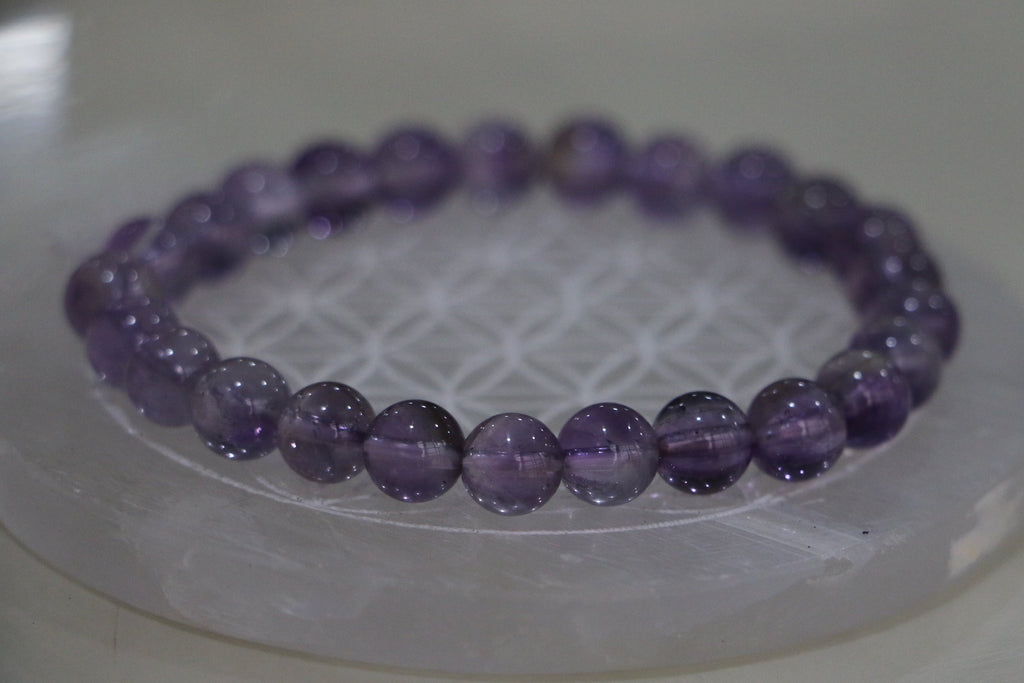 Purple beaded bracelet on a white circular stand with a light background