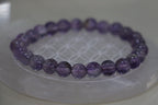 Purple beaded bracelet on a white circular stand with a light background