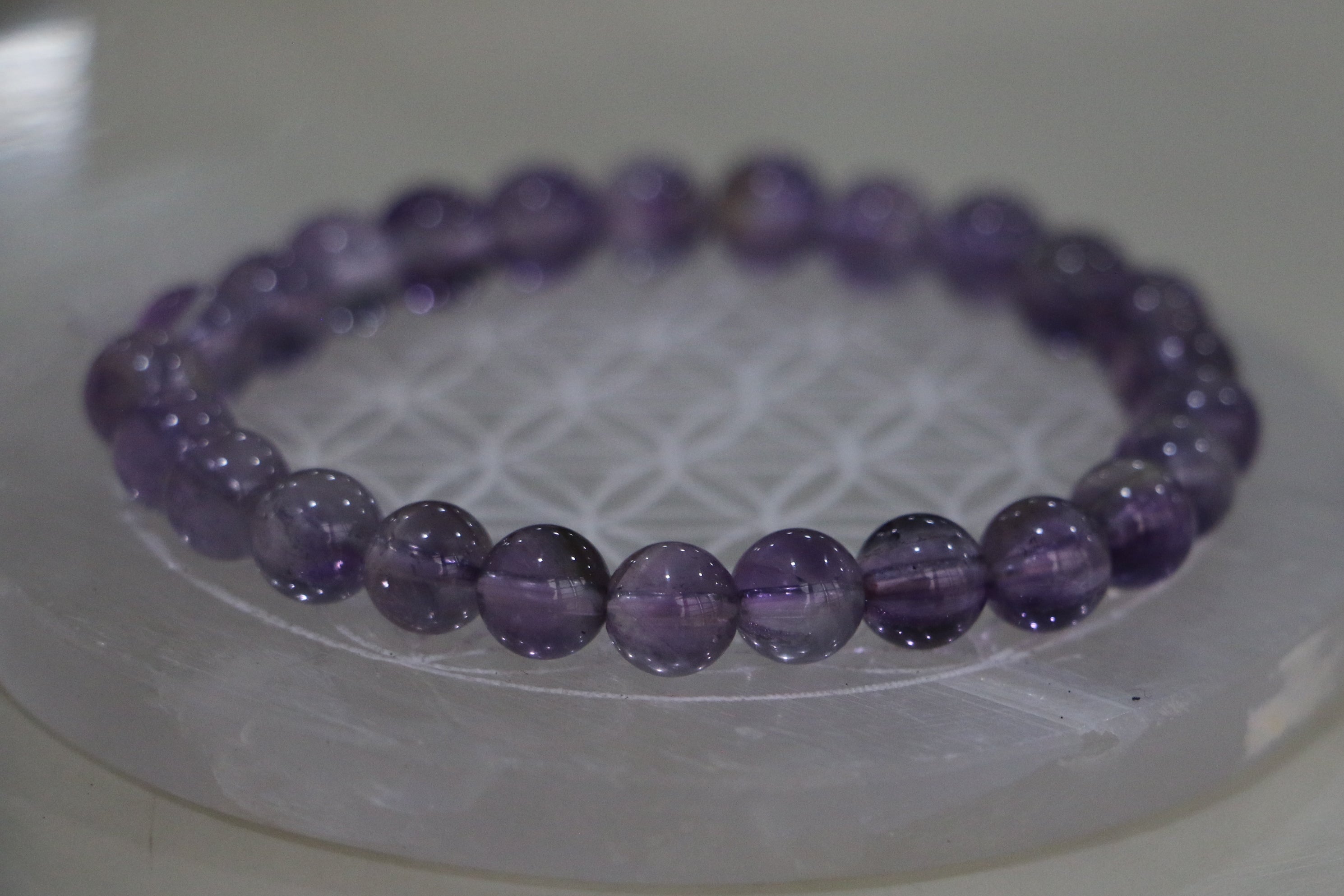 Purple beaded bracelet on a white circular stand with a light background
