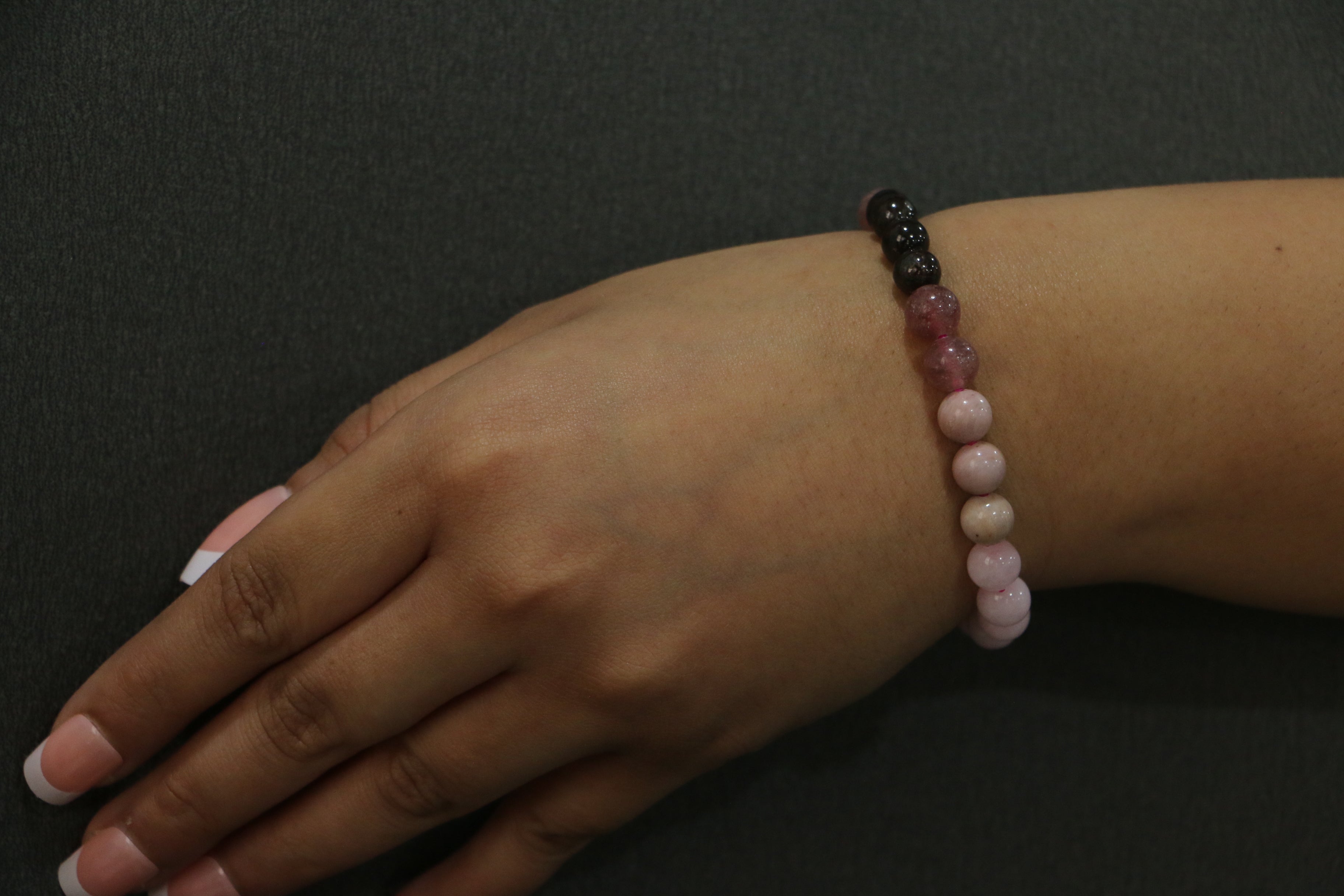 Hand wearing a beaded bracelet on a dark background